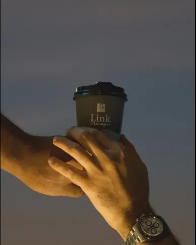 A Link Lounge takeaway cup held up against the evening sky